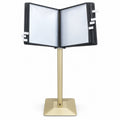 Gold floor-standing flip display stand with black-framed document pockets open for browsing and index tabs along the sides.